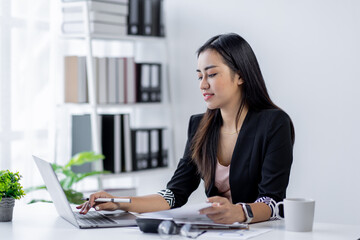 Asian Businesswoman Using laptop computer and working at office with calculator document on desk, doing planning analyzing the financial report, business plan investment, finance analysis concept.
