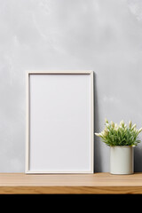 Blank vertical picture frame mockup hanging on a plain wall with wooden desk table and flower vase