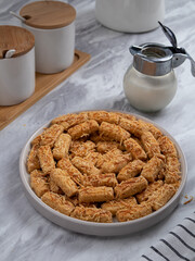 Kue Kastengel or Kaastangels are neatly presented on a white plate with attractive decorations. They are isolated against a kitchen background.
