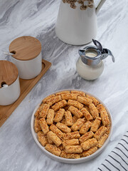 Kue Kastengel or Kaastangels are neatly presented on a white plate with attractive decorations. They are isolated against a kitchen background.