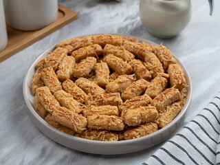 Kue Kastengel or Kaastangels are neatly presented on a white plate with attractive decorations. They are isolated against a kitchen background.