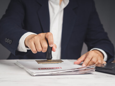 Businessman in a suit stamped for rejected documents while sitting at the table.