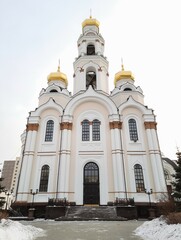 Fototapeta na wymiar White Orthodox Church in Russia with golden domes and bell tower