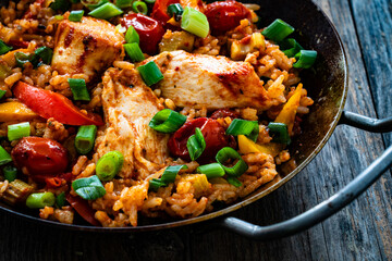 Jambalaya one pot dish - fried chicken breasts with white rice, tomatoes, bell pepper and celery on wooden table
