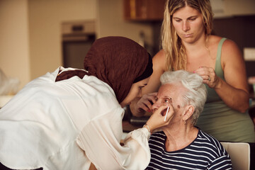 In this heartwarming real-life scene, a girl in a hijab and her sister lovingly apply makeup to their elderly grandmother, preparing her for a special family anniversary celebration, showcasing the