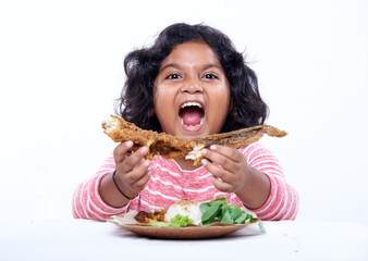 Little asian girl eating crunchy Fried Fish with rice and vegetable