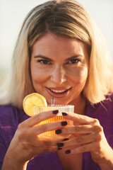 A beautiful blonde woman enjoys a cocktail on a charming outdoor terrace, showcasing her real and unretouched beauty, with a captivating and unprocessed portrait