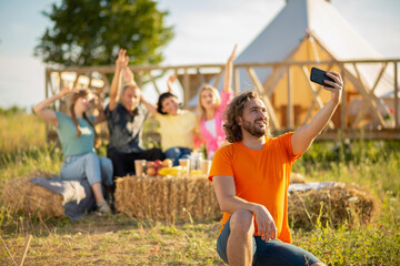 Obraz premium Sunny summer day group of multiracial friends meeting all together at campsite they chilling and taking selfie pictures with smartphone while sitting on the haystack