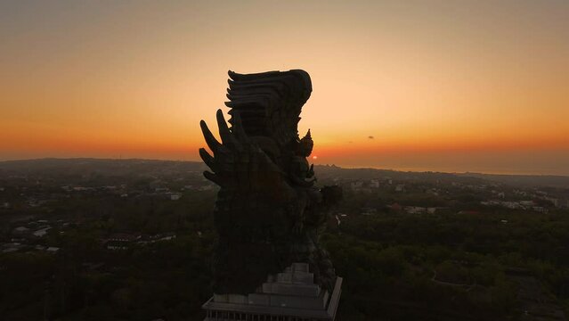 Aerial view of the park with the GWK statue during sunset. The sun sets below the horizon and illuminates the statue with golden light. Must-see attractions in Bali.