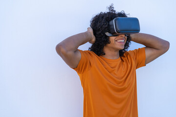 A young man with afro hair enjoying virtual reality glasses wearing a bright orange t-shirt on a white background.