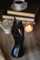 Vintage books, reading glasses, gold pen, hand model, gold jewelry, scented candles, flowers, chess pieces and cup of tea or coffee on the table. Dark academia concept. Selective focus.