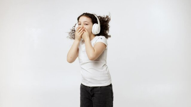 Smiling child listening to music on a light background, smiling little girl wearing headphones having fun with music. Happy childhood concept.