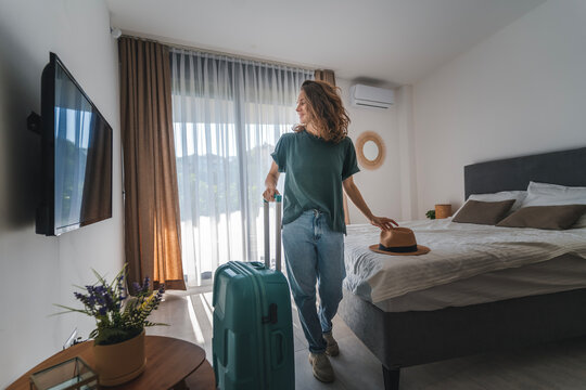 A young woman in a hat with a suitcase check in a hotel room. Booking and Accommodation travel concept