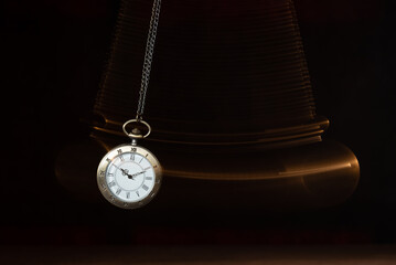 Hypnosis session. Vintage pocket watch with chain swinging over surface on dark background among...