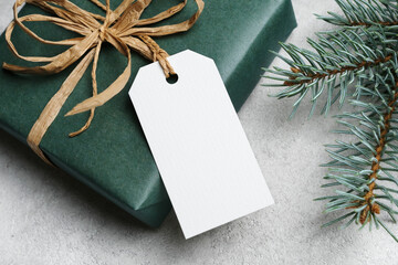 Blank gift tag card mockup with christmas gift box on grey background, white label with copy space...