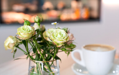 Beautiful roses in a vase and a cup of cappuccino on a table in a cafe. Close-up. Selective focus.