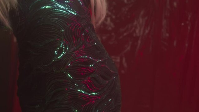 Midsection of unrecognizable drag queen in shiny mini dress dancing on stage during drag show at night club