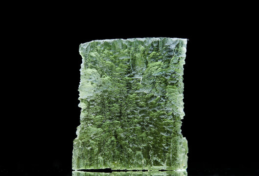 Moldavite stone isolated on black background. Close up of a green precious Czech gemstone. Genuine natural tektite glass.