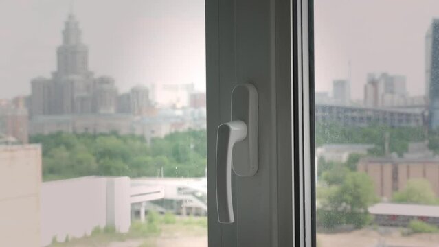 A hand closes a window in an apartment or house. 