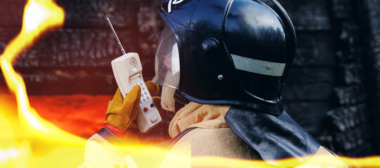 Concept call to rescue service banner. Portrait firefighter officer talking on radio walkie talkie with colleagues background wooden house in fire