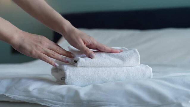 Close-up of hands putting stack of fresh white bath towels on the bed sheet. Room service maid cleaning hotel room