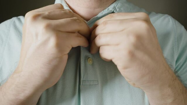 Male hands fasten buttons on a blue polo shirt