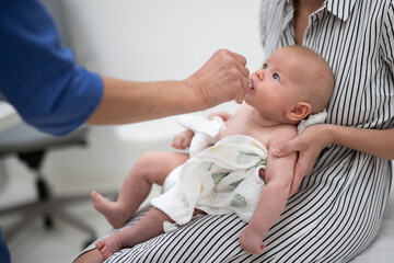 Pediatrician administring oral vaccination against rotavirus infection to little baby in presence of his mother. Children health care and disease prevention. - 659933603