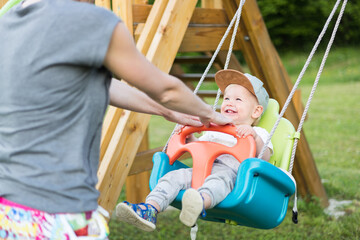 Mother pushing her infant baby boy child on a swing on playground outdoors