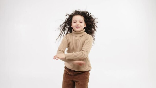 Smiling child dancing on a light background, smiling little girl dancing, having fun to the music. The concept of a cheerful and carefree childhood