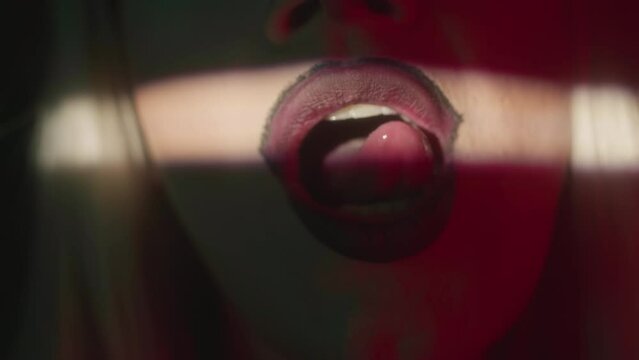 Closeup of eccentric drag queen making air kiss at camera and licking her upper lip with tongue seductively on dark background
