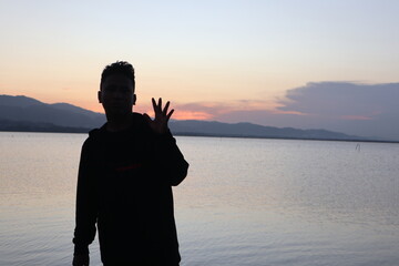 Silhouette of a young man standing by the lake enjoying the sunset. peaceful atmosphere in nature
