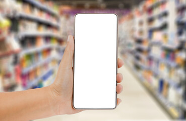 Hand holding a smartphone on blurred market background. Transparent mobile screen mockup. Shopping online or technology concept.