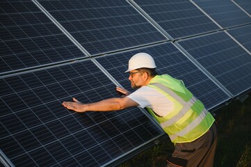 Side view of male worker installing solar modules and support structures of photovoltaic solar array.