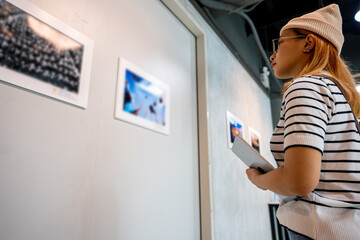Fototapeta na wymiar Asian woman holding tablet at art gallery collection in front framed paintings pictures on white wall, Young person at photo frame hold digital book leaning against at show exhibition artwork gallery