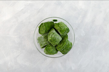 Crushed green spinach shock frozen in form of briquettes on grey textured background, top view. Fresh frozen food. Smart solution for storing greenery