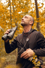 Man using binoculars and camera for birdwatching and other observing animals in nature.