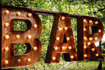 Bar signboard. Inscription from large metal letters decorated with glowing light bulbs. - obrazy, fototapety, plakaty