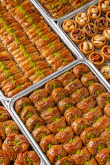 Different types of freshly baked baklava in baking trays. Turkish desert with peanut, pistachio for holiday or ramadan. Traditional Middle Eastern Flavors. Selective focus, pattern.