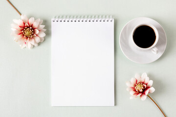 Composition with opened blank notepad, cup of black coffee, dahlia flowers on a gray background. Festive office desktop concept. Morning coffee cup.