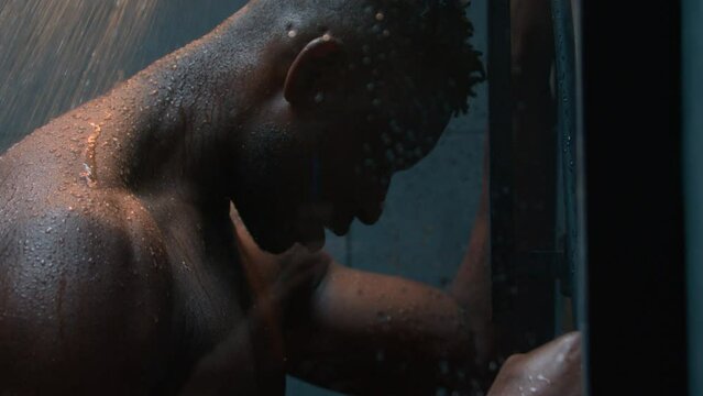 Tired depressed African American naked powerful man under falling water in shower angry guy hitting wall post workout stress impotence anxiety pain think problem crisis male washing body care hygiene