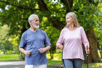Senior man and woman in sportswear running in the park and doing nordic walking. They lead a...