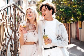 Young smiling beautiful woman and her handsome boyfriend in casual summer clothes. Happy cheerful family. Female having fun. Couple posing in street. Holding and drinking cocktail drink in plastic cup