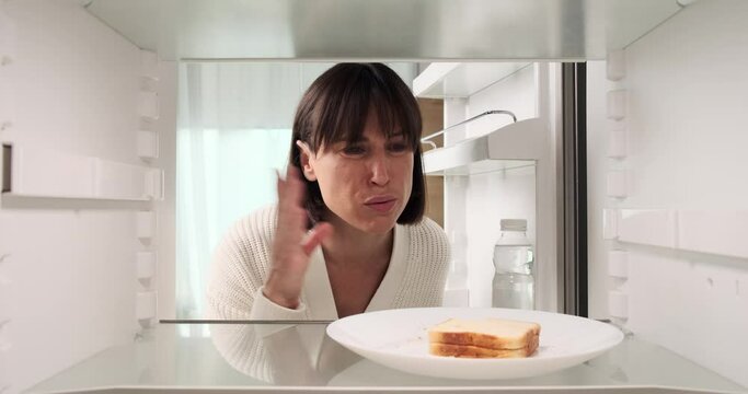 A woman expresses her discontent upon discovering the unpleasant odor of a spoiled sandwich in the refrigerator. Her reaction reflects her disappointment with the spoiled food item.