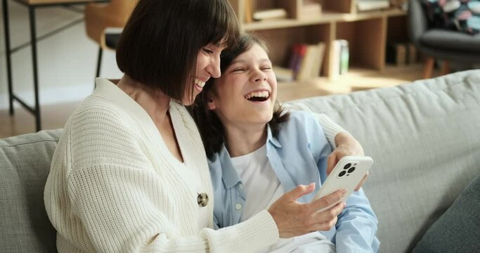 A mother and son share laughter and use a phone while sitting on the living room couch. Their joviality adds a sense of warmth and connection to the room.