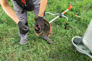Man pulls the line out of the weed trimmer coil - maintenance of garden tools.