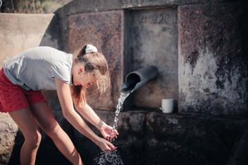 a caucasian  girl drinks, collects water with her palms from a cold spring hidden deep in the...