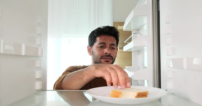Contented Middle Eastern man retrieves an apple from the refrigerator and takes a satisfying bite. His joyful act of enjoying a fresh and healthy snack reflects the simple pleasures of life.