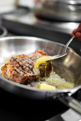 Professional chef cooking beef steak in frying pan on stove in restaurant kitchen