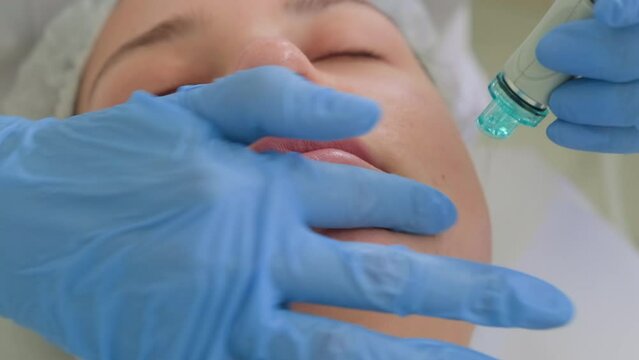 Beautician in gloves conducts vacuum cleaning and polishing face skin of young woman in cosmetology clinic. Professional hardware procedures. Hydrafacial massage process.