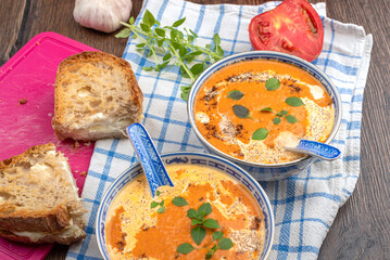 Slices of bread with soft cheese, tomato puree soup with cream and green basil leaves.